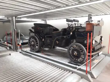 Een vintage zwarte auto met koperen accenten staat op een platform in de moderne, uit meerdere verdiepingen bestaande parkeergarage Classic Remise.