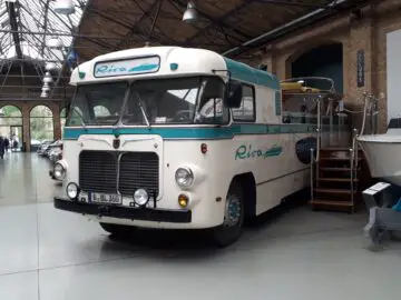 Binnen bij Classic Remise staat een vintage Riva-bus tentoongesteld, compleet met een boot eraan.