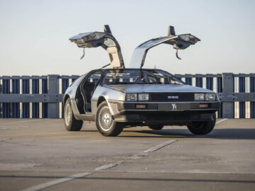 Een roestvrijstalen DeLorean met zijn iconische vleugeldeuren open staat op klaarlichte dag geparkeerd op een parkeerplaats op het dak en geeft de essentie van futuristisch design weer.