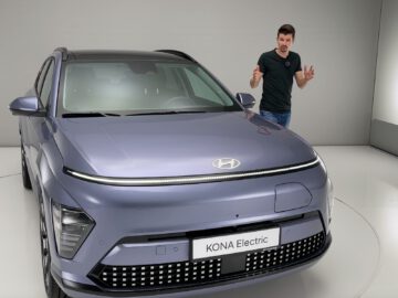 Een man staat naast een metallic blauwe Hyundai KONA Electric in een minimalistische studio met witte muren en vloer.