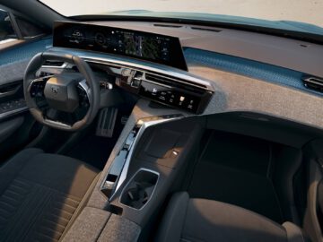 Binnenaanzicht van een moderne Peugeot, met het futuristische interieur van de nieuwe e-3008 met een strak dashboard met digitale displays, een stuur en stoelen in donkere stof. De middenconsole is voorzien van een versnellingspook en diverse bedieningsknoppen.