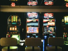 Een rij verlichte gokautomaten met verschillende displays en vier lege stoelen ervoor, geplaatst in een slecht verlicht casino, belicht enkele van de populairste casinospellen.