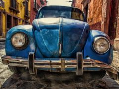 Close-up van de voorkant van een blauwe vintage Volkswagen Kever, geparkeerd in een geplaveide straat met kleurrijke gebouwen op de achtergrond, wat een van de vele redenen voor WA kapitaal laat zien.