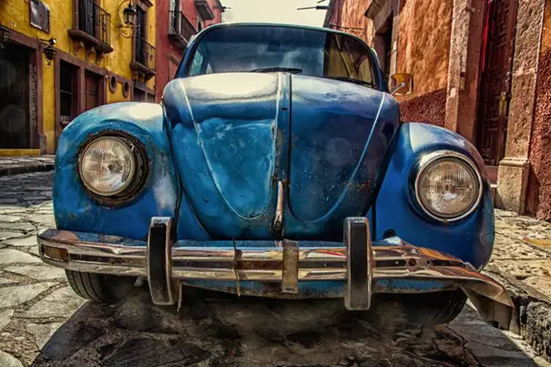 Close-up van de voorkant van een blauwe vintage Volkswagen Kever, geparkeerd in een geplaveide straat met kleurrijke gebouwen op de achtergrond, wat een van de vele redenen voor WA kapitaal laat zien.