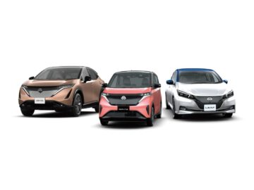 Drie Nissan EV’s staan achter elkaar geparkeerd. Van links naar rechts zijn dit de Ariya, Sakura en Leaf. De Ariya is bruin, de Sakura is rood en de Leaf is wit met een blauw dak.