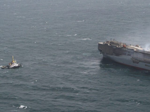 De sleepboot nadert de Fremantle Highway met rook die uit de boeg komt, gezien op open zee met schokkerige golven, wat duidt op een mogelijk brandscenario of een reddingsoperatie.