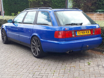 Een blauwe Audi S6-stationwagen staat geparkeerd in een geplaveide straat, met op de achterste kentekenplaat duidelijk zichtbaar "12-HH-KR".