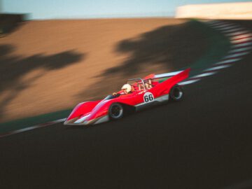 Een rode Lotus Type 66-raceauto met het nummer 66 snelt rond een gebogen baan, waarbij een vage omgeving beweging aangeeft.