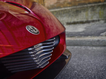 Close-up van de grille en het logo van een rode Alfa Romeo 33 Stradale geparkeerd op straat.