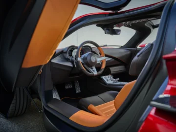 Het interieur van de moderne Alfa Romeo 33 Stradale-sportwagen is voorzien van oranje en zwart lederen stoelen, een geavanceerd dashboard en een sportief stuur. De linkerzijdeur is open en onthult het luxe, strakke ontwerp.