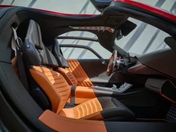 Binnenaanzicht van een moderne sportwagen, die doet denken aan de Alfa Romeo 33 Stradale, met zwart en oranje lederen stoelen, een strak dashboard en een futuristisch stuur, met het dak en de deur gedeeltelijk open.