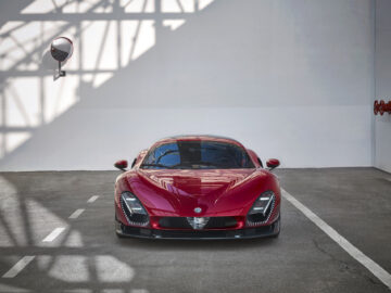 Op een ruime, overdekte parkeerplaats met witte muren en aan de linkermuur een spiegel gemonteerd staat een Alfa Romeo 33 Stradale geparkeerd.