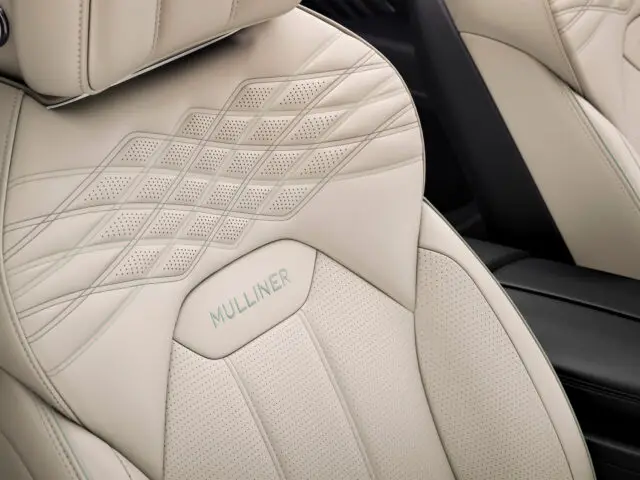 Close-up van luxe beige lederen autostoelen met diamantstiksels en perforatiepatronen, met 'Mulliner'-borduurwerk op de rugleuning, in de Bentley Bentayga EWB Mulliner.