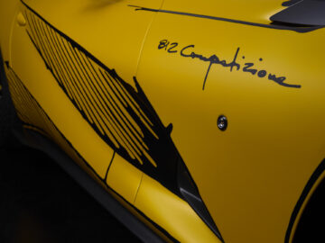 Een close-up van de zijkant van een gele Ferrari 812 Competizione sportwagen met zwart grafisch ontwerp en de tekst "812 Competizione" op de carrosserie.