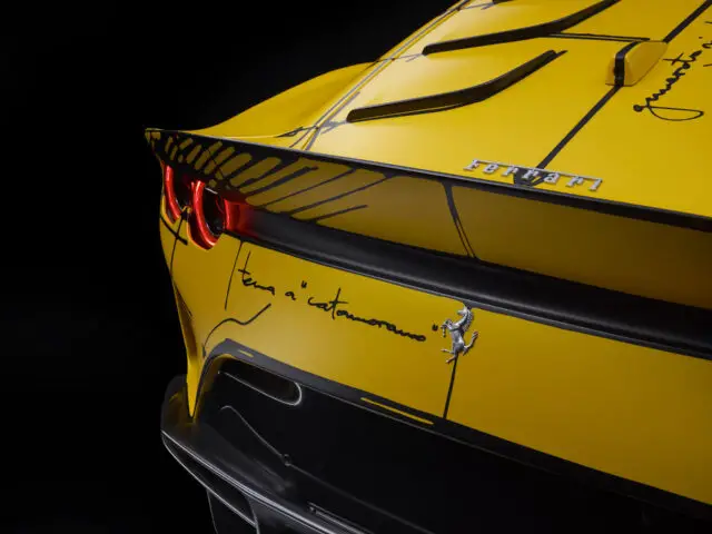 Close-up van de achterkant van een gele Ferrari 812 Competizione-sportwagen met opvallende zwarte handtekeningen en een Ferrari-logo op een strak, aerodynamisch ontwerp.