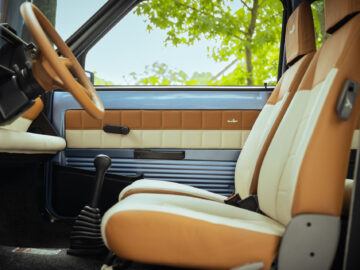 Interieur van een Fiat Panda 4x4 Piccolo Lusso met beige en wit lederen stoelen, een zwarte versnellingspook en een zwarte handgreep op het deurpaneel met groen blad zichtbaar buiten het raam.