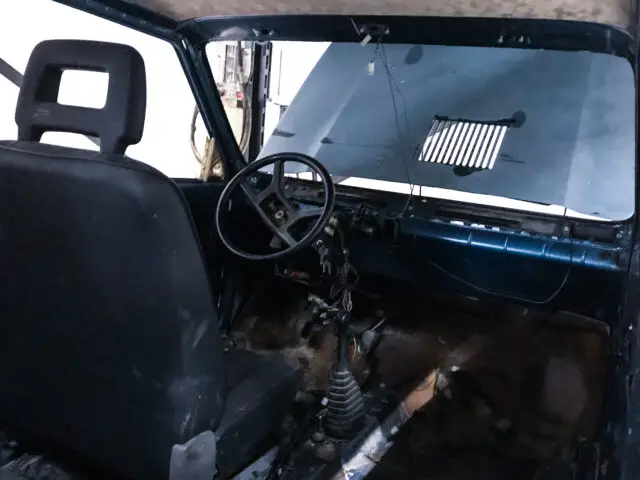 Interieur van een stoffige, oude Fiat Panda 4x4 Piccolo Lusso met een versleten bestuurdersstoel, stuurwiel, dashboard met ontbrekende onderdelen en versnellingspook. De voorruit ziet er vuil uit en het voertuig heeft geen vloer.