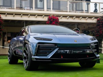 Een strakke, blauwe Lamborghini Lanzador SUV staat geparkeerd op een verzorgd gazon voor een gebouw, met rode bloemen op de achtergrond.