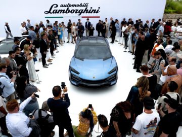 Een menigte verzamelt zich rond de opvallende blauwe Lamborghini Lanzador SUV, elegant tentoongesteld op een wit platform tijdens een auto-evenement.