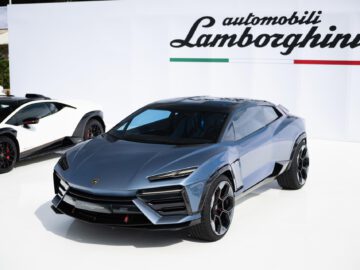 Een blauwe Lamborghini Lanzador SUV wordt op een autoshow getoond naast een witte Lamborghini-sportwagen, met een bord "automobili Lamborghini" op de achtergrond.