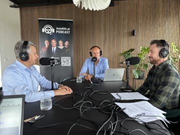 Drie mannen met een koptelefoon nemen AutoRAI Podcast #17 op. Ze zitten rond een tafel met microfoons, laptops en papieren. Op de achtergrond staat een podcast-promotieposter.