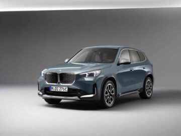 Een BMW ix1 SUV staat geparkeerd in een goed verlichte studio tegen een grijze achtergrond. Het blauwe voertuig laat zijn opvallende grille en moderne design naadloos zien.