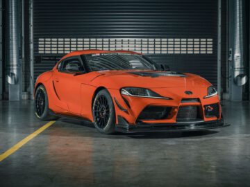 Een felrode Toyota GR Supra GT4 100 Edition-sportwagen in een garage met zwarte wielen en een strak ontwerp, geparkeerd op een betonnen vloer tegen een grote metalen sluiter.