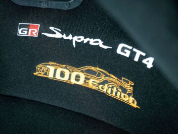 Close-up van een zwarte stoel met geborduurde logo's met de tekst "Toyota GR Supra GT4 100 Edition" in wit en goud, samen met een omtrek van een raceauto.