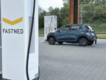 Een blauwe Dacia Spring Electric SUV staat geparkeerd en wordt opgeladen bij een laadstation voor elektrische voertuigen van Fastned.