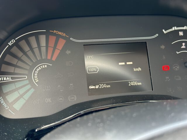 Het Dacia Spring Electric autodashboard toont een volle batterij bij 100%, een resterende actieradius van 204 km en een totale afgelegde afstand van 2406 km. De temperatuur bedraagt 23°C.