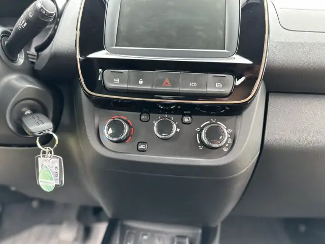 Close-up van het dashboard van een Dacia Spring Electric met knoppen voor de klimaatregeling, de knop voor de alarmlichten en een sleutel in het contactslot.