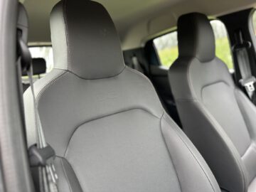 Close-up van de voorstoelen in een moderne Dacia Spring Electric met grijze bekleding en zichtbare stiksels.