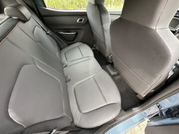 Achterbankaanzicht van een Dacia Spring Electric met grijze bekleding en twee voorstoelen zichtbaar. Het interieur oogt schoon en ruim, met een deur aan de linkerkant.