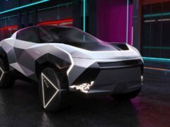 Een futuristisch, hoekig elektrisch voertuig van Nissan staat geparkeerd in een natte stadsstraat, verlicht door neonlichten.