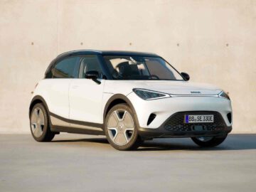 Een strakke, witte elektrische compacte SUV met vijfspaaks wielen en donker getinte ramen staat netjes geparkeerd voor een beige betonnen muur.