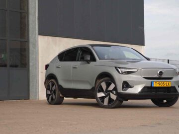 Een zilverkleurige Volvo C40 SUV staat geparkeerd op een verhard oppervlak nabij een groot gebouw met ramen. Het voertuig heeft een geel kenteken met het nummer "T-905-LX.