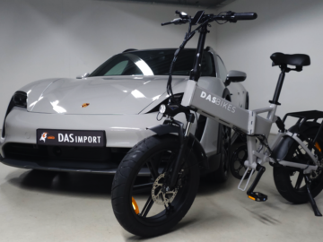 Een zilveren elektrische fatbike met het opschrift "DAS BIKES" staat geparkeerd voor een zilveren sportwagen met een "DAS IMPORT" kenteken, waardoor de snelgroeiende markt van Das Automotive in een goed verlichte binnenruimte wordt benadrukt.