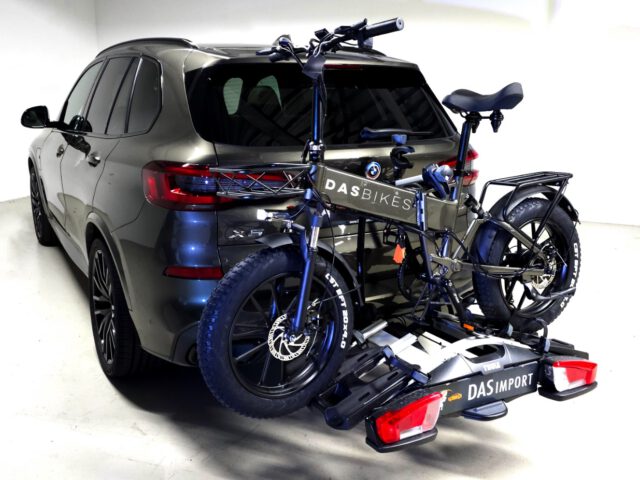 Een donkergekleurde SUV van Das Automotive is uitgerust met een fietsenrek aan de achterzijde waarop twee elektrische fatbikes veilig kunnen worden geplaatst. De kamer is helder verlicht met witte muren en een lichtgekleurde vloer, wat het strakke ontwerp en de prestatiebereidheid voor de snelgroeiende markt benadrukt.