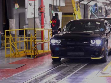 Een strakke zwarte Dodge Challenger SRT glijdt langs een lopende band in de fabriek, met toegewijde werknemers in de buurt.