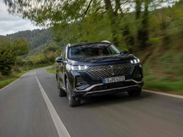 Een zwarte SUV van Wey 03 rijdt op een bochtige weg omgeven door groen en bomen.