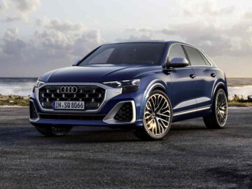 Een blauwe Audi SQ8 SUV staat geparkeerd op een kustweg aan zee onder een bewolkte hemel.