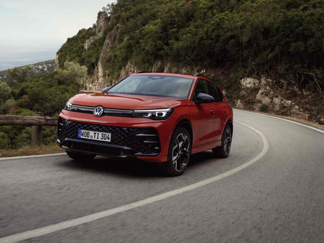 Een rode Volkswagen Tiguan SUV rijdt op een bochtige bergweg omringd door bomen en rotsen.