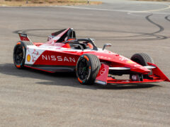 Een rood-witte Nissan Formule E-auto geparkeerd op een verhard oppervlak, met sponsorlogo's van Shell, Nismo en anderen.