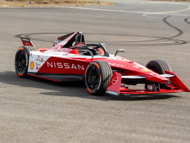 Een rood-witte Nissan Formule E-auto geparkeerd op een verhard oppervlak, met sponsorlogo's van Shell, Nismo en anderen.