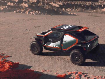 Dacia's terreinwagen, met een robuust ontwerp en gedurfde kleuren, rijdt vol vertrouwen over een droog, gebarsten woestijnterrein met rotsformaties en schaarse vegetatie op de achtergrond.