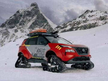 Een rood Nissan X-Trail Mountain Rescue-voertuig met rupsbanden staat geparkeerd in een met sneeuw bedekt bergachtig gebied, met de ruige schoonheid van een met sneeuw bedekte berg op de achtergrond.
