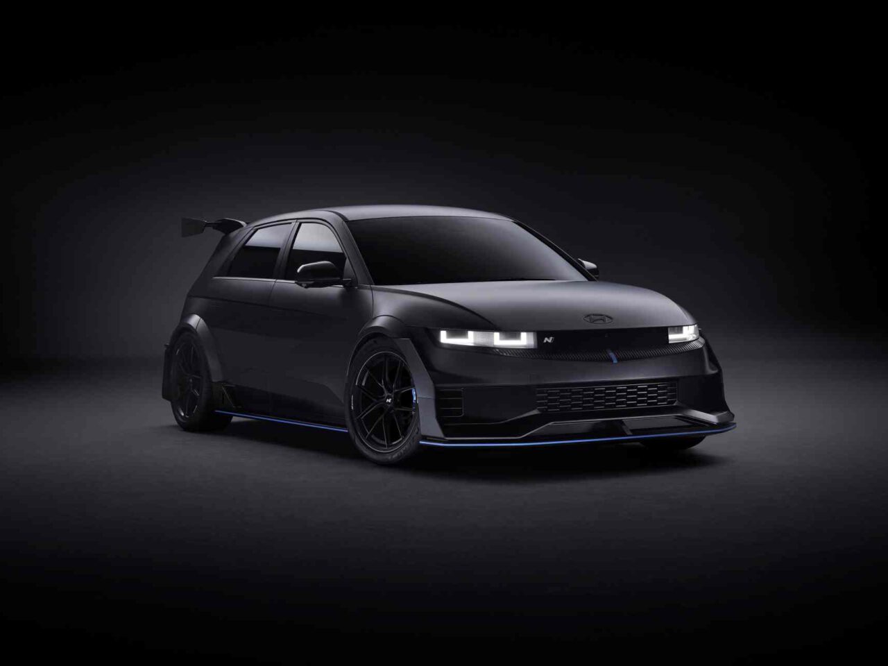 Een zwarte, futuristische elektrische auto Ioniq 5 met een strak ontwerp, verlichte koplampen, aerodynamische kenmerken en een achterspoiler wordt tentoongesteld tegen een donkere achtergrond.