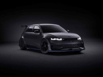 Een zwarte, futuristische elektrische auto Ioniq 5 met een strak ontwerp, verlichte koplampen, aerodynamische kenmerken en een achterspoiler wordt tentoongesteld tegen een donkere achtergrond.