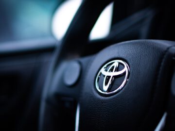 Close-up van een Toyota-stuur met het bedrijfslogo, een voorbeeld van een van de betrouwbaarste gelegenheden op de markt. Het zwarte interieur van het voertuig is enigszins wazig op de achtergrond.