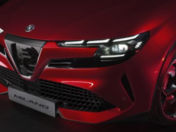 Nahaufnahme der Front eines roten Alfa Romeo Sportwagens, wobei die Scheinwerfer, der Kühlergrill und die Plakette hervorgehoben werden.
